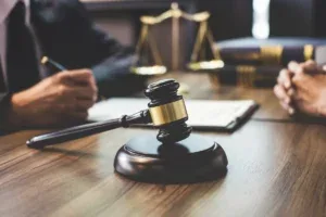 Advogados sentados à mesa, com malhete e balança de têmis